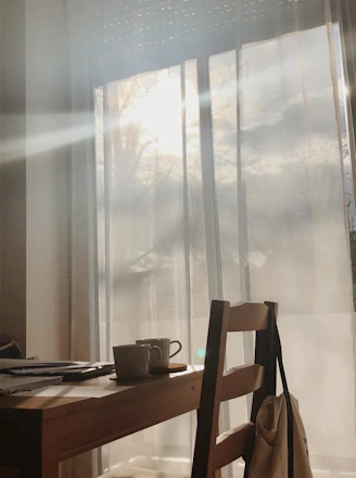 Soft morning light filters through a calm, cozy interior with a cup of coffee on a wooden desk.