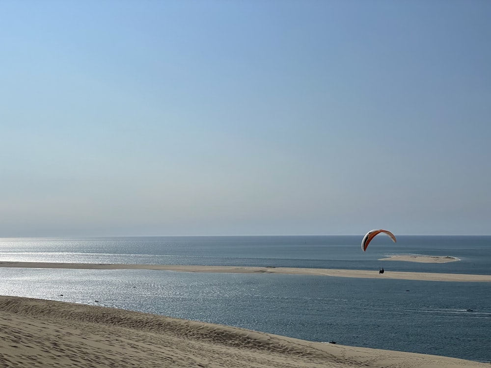 person in orange and yellow parachute over the sea during daytime