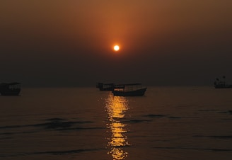 A serene sunset casting golden light over calm waters dotted with anchored boats.