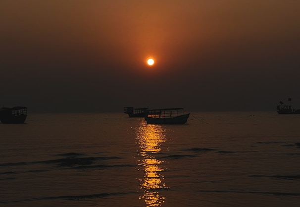 A serene sunset casting golden light over calm waters dotted with anchored boats.