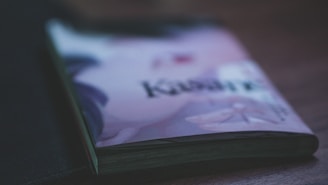 A close-up of a slightly closed book or magazine on a wooden surface with an illustration and text on its cover, featuring soft lighting and a shallow depth of field.
