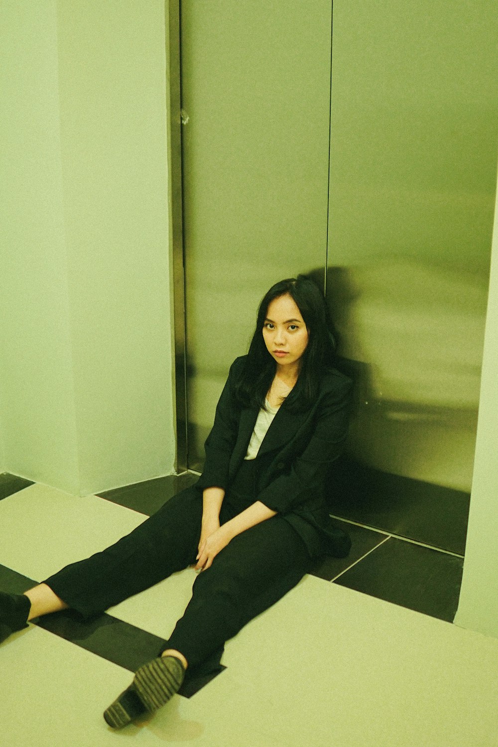 woman in black blazer and black pants sitting on white floor tiles