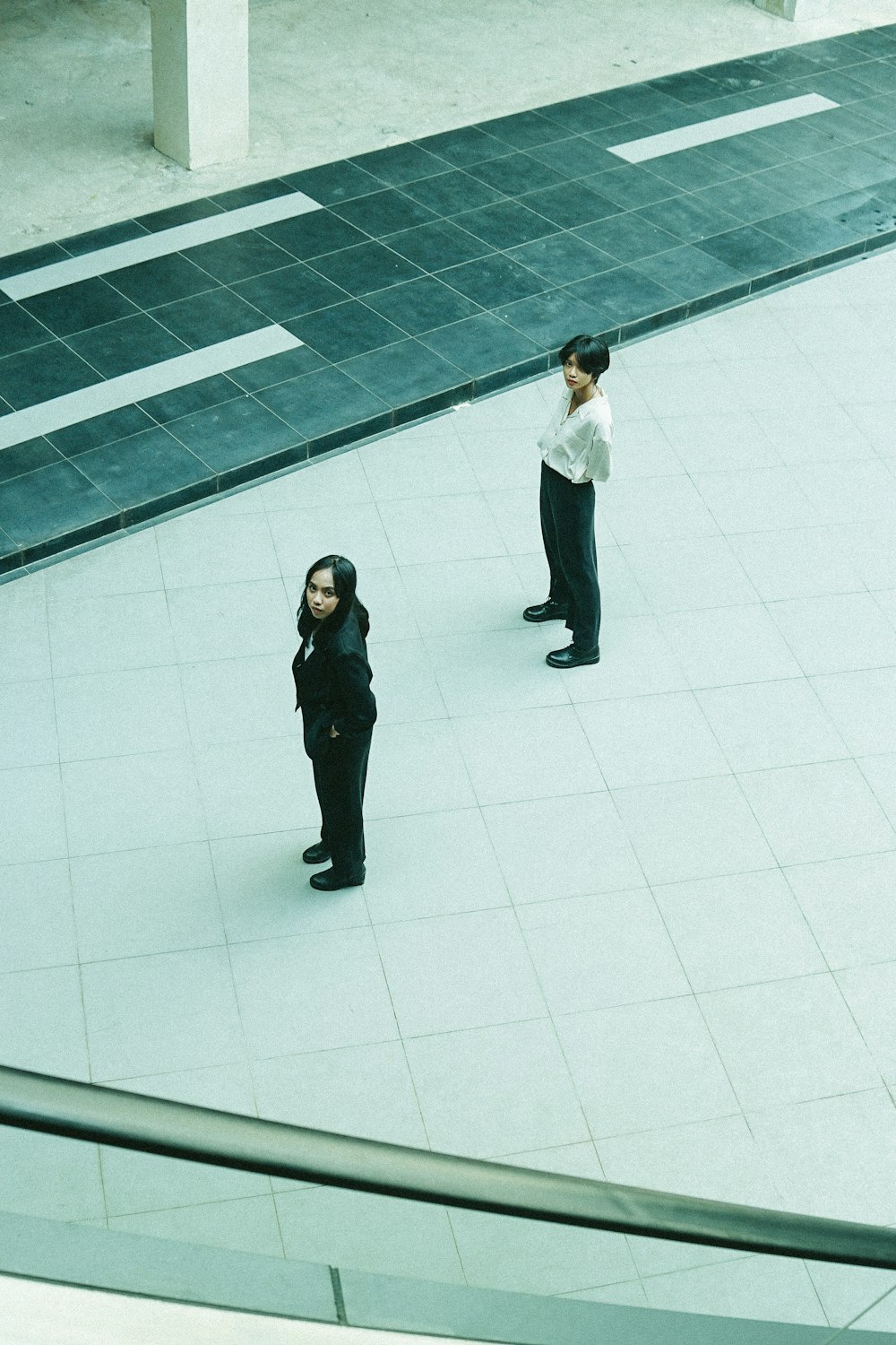 2 women in white dress shirt and black pants standing on white floor tiles