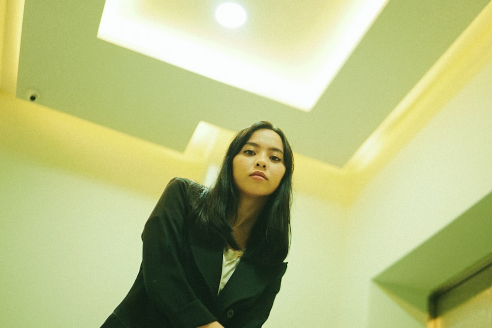 woman in black coat standing near white wall