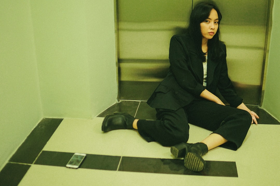 woman in black coat sitting on white ceramic floor tiles