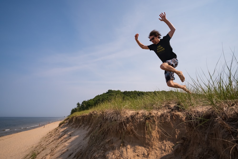 Mann in schwarzem T-Shirt und schwarzen Shorts springt tagsüber auf braunen Felsen