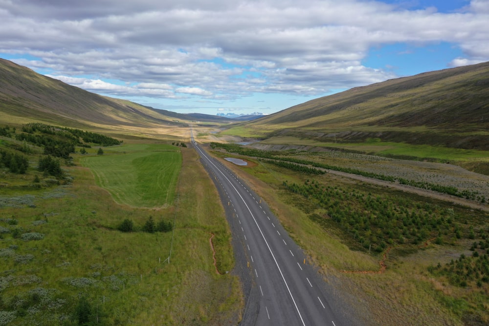 estrada de asfalto cinza entre o campo de grama verde sob nuvens brancas e céu azul durante o dia