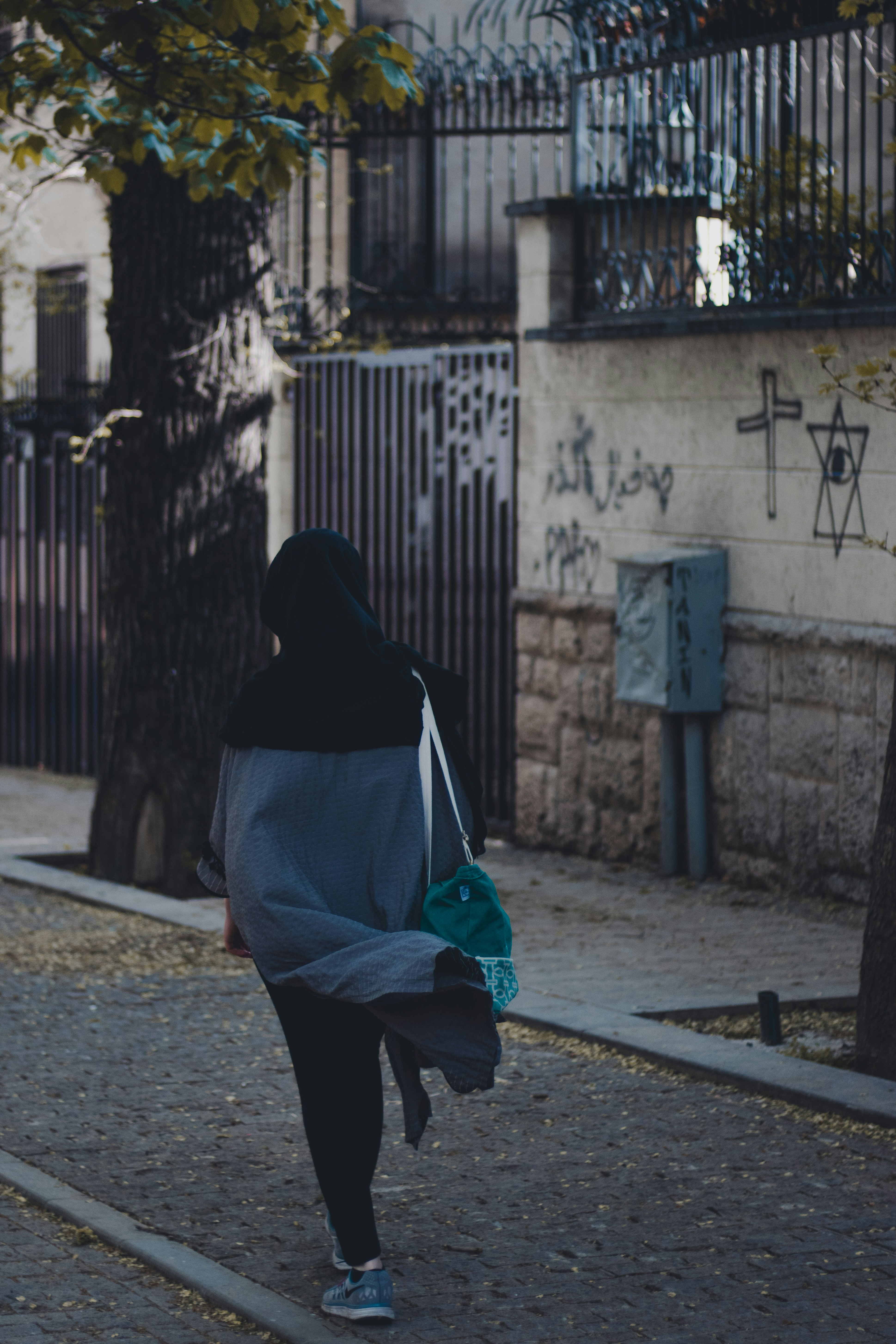 woman in black hijab and black pants walking on sidewalk during daytime