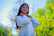 A smiling woman outdoors taking a deep, refreshing breath surrounded by green trees.