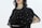 A person is wearing a black embellished garment with intricate embroidery, featuring delicate beadwork and patterns. The attire includes a semi-transparent fabric overlay adorned with decorative designs. The background is plain, highlighting the outfit's details.