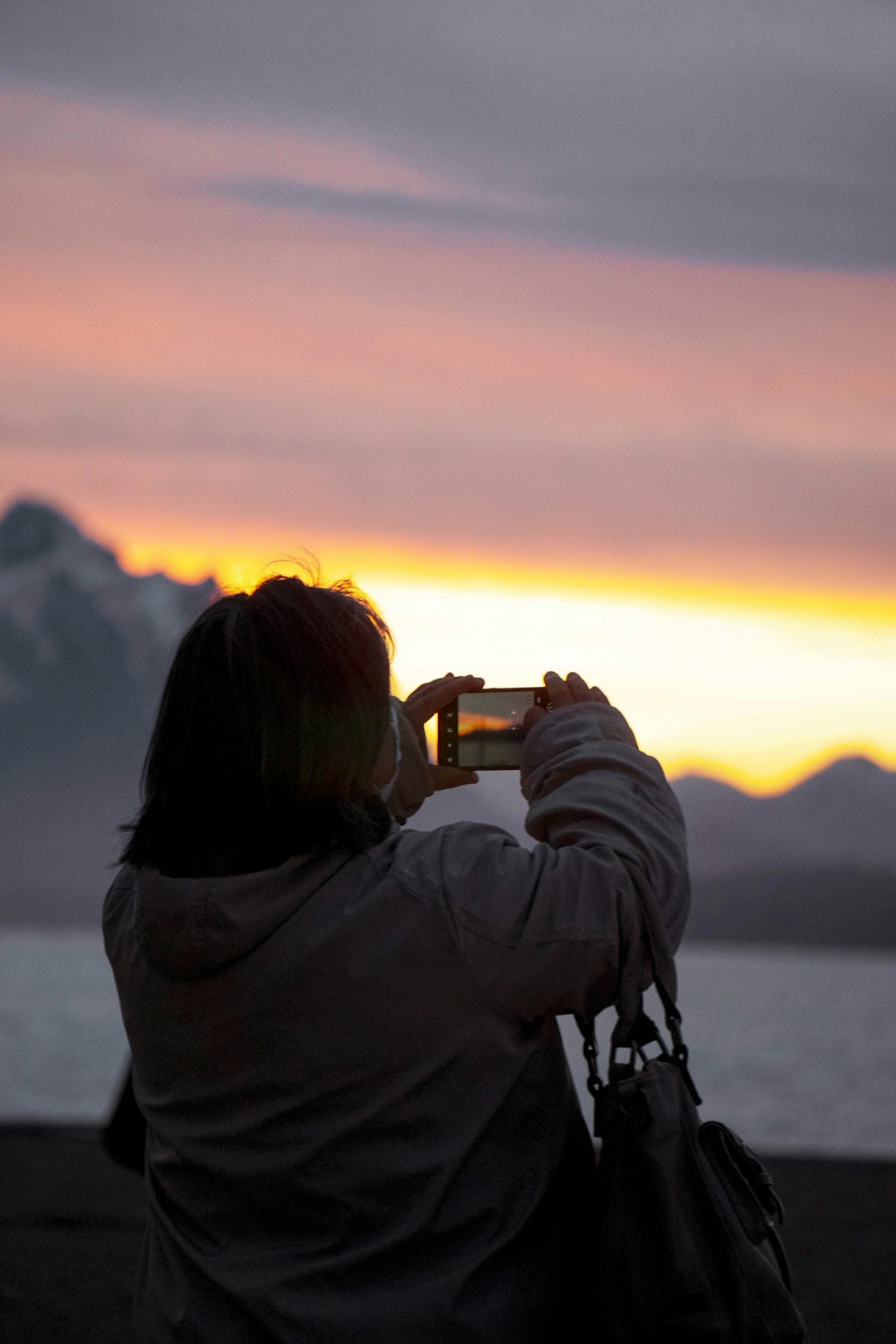 woman in gray hoodie taking photo of sunset