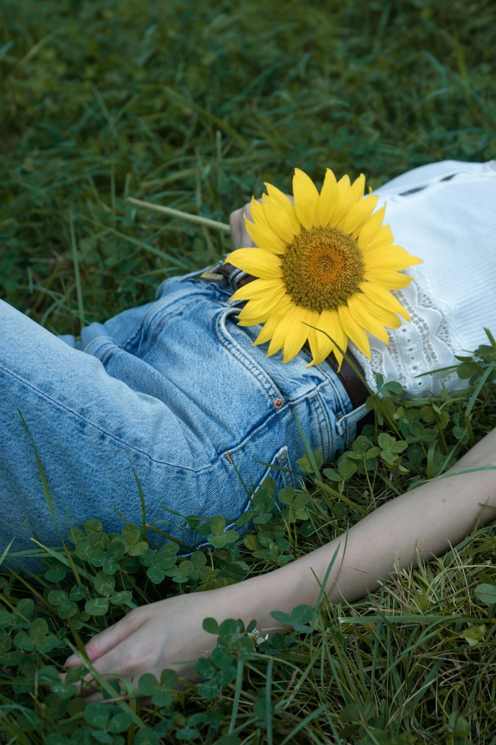 person in blue denim jeans sitting on white textile with yellow sunflower on her lap