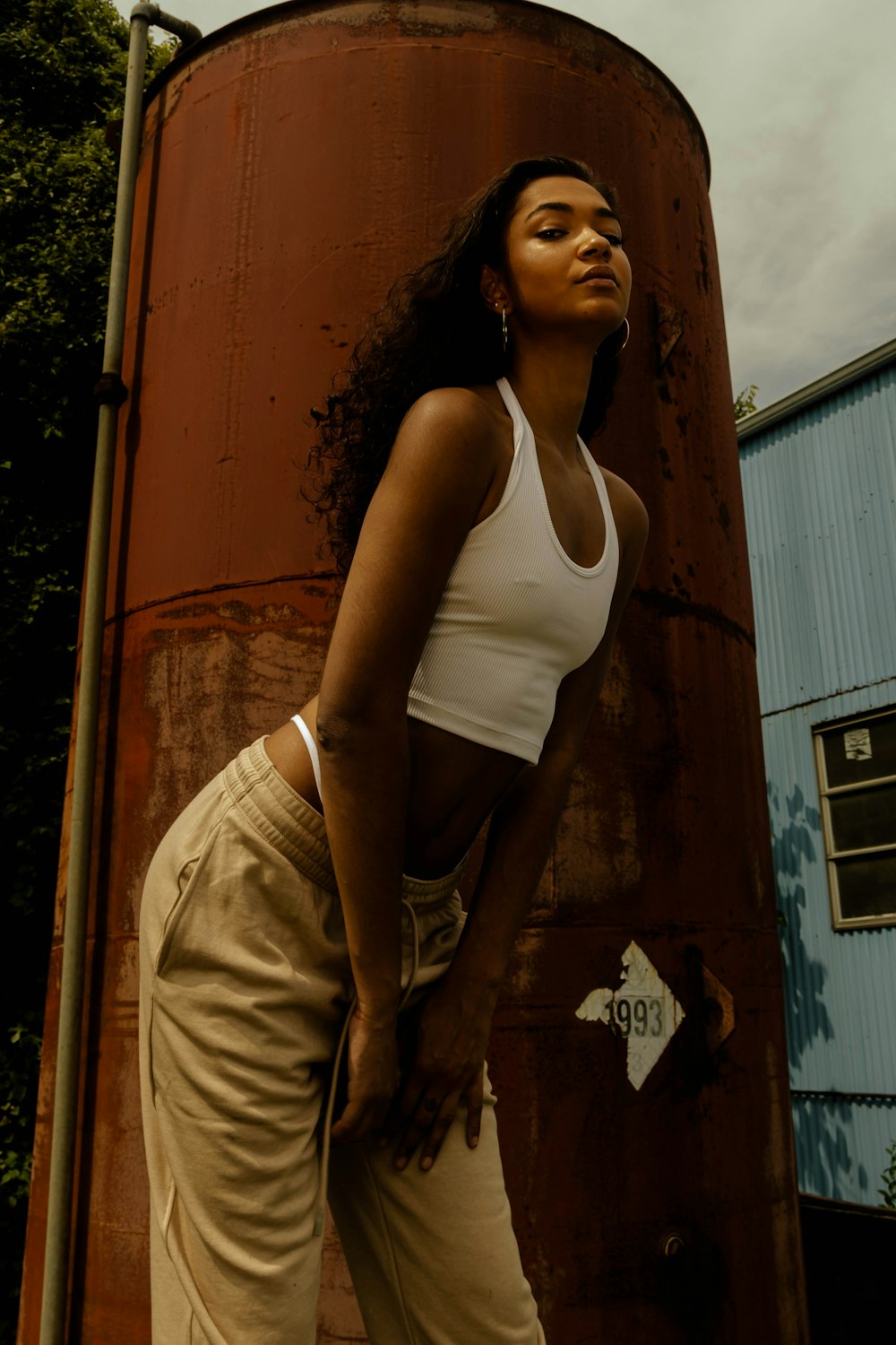 woman in white tank top and brown pants standing beside yellow wall