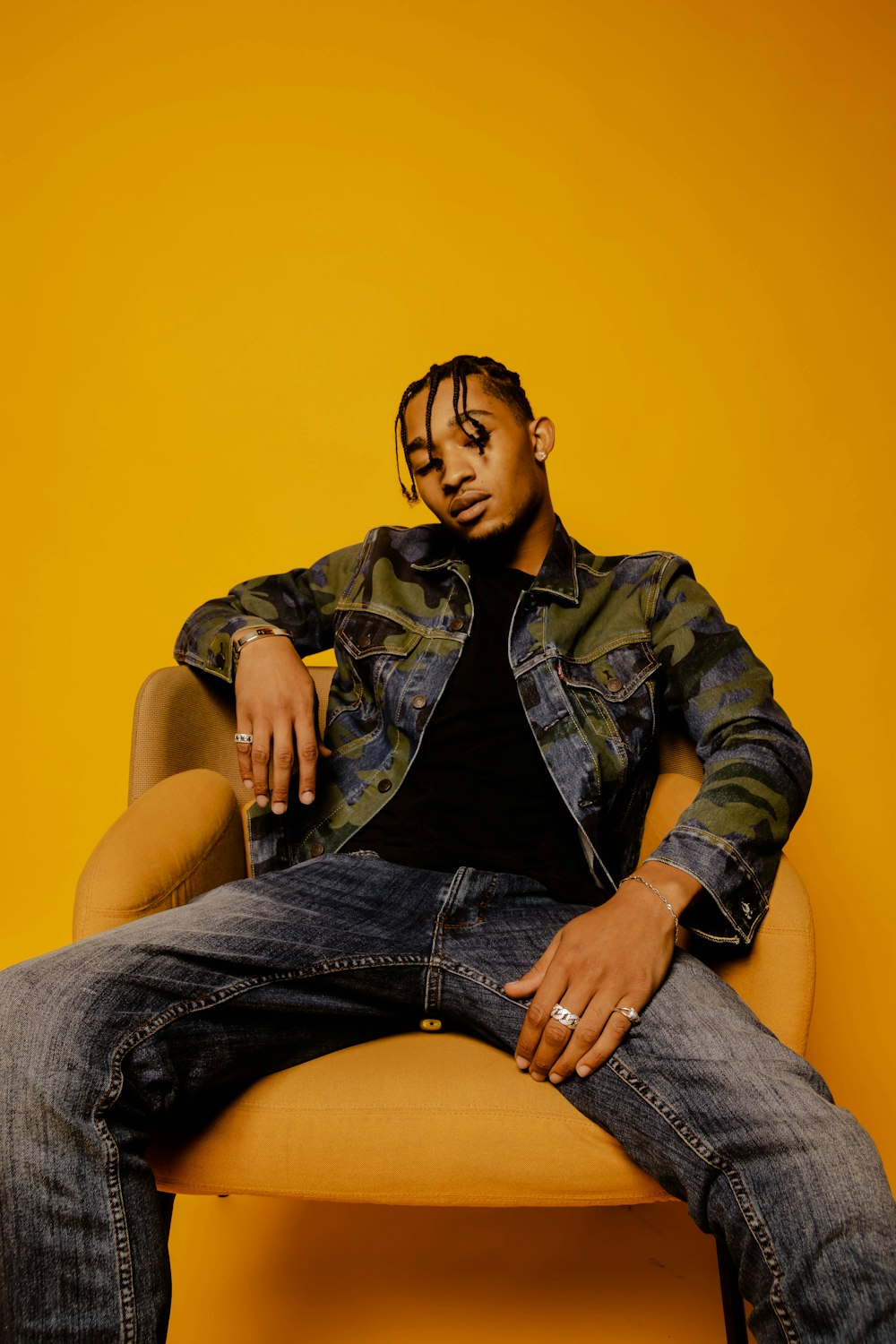 man in green and black camouflage jacket and blue denim jeans sitting on yellow chair