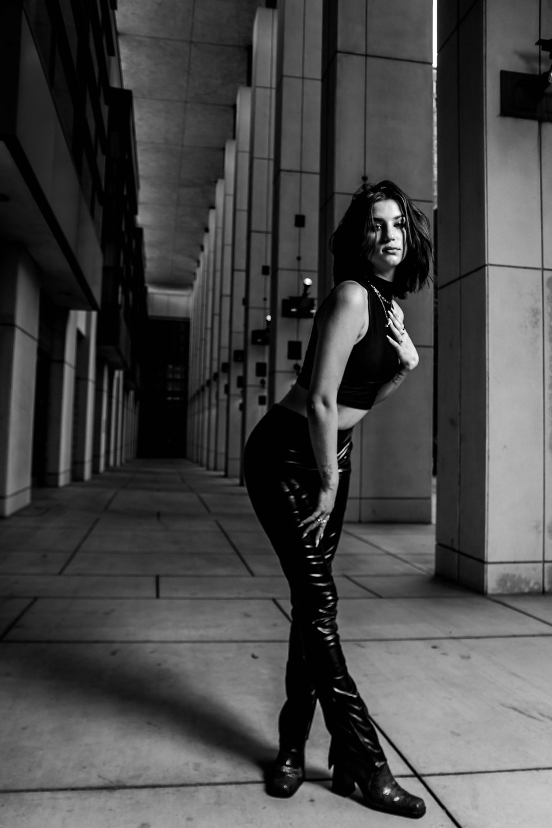 woman in white tank top and black pants standing on sidewalk in grayscale photography
