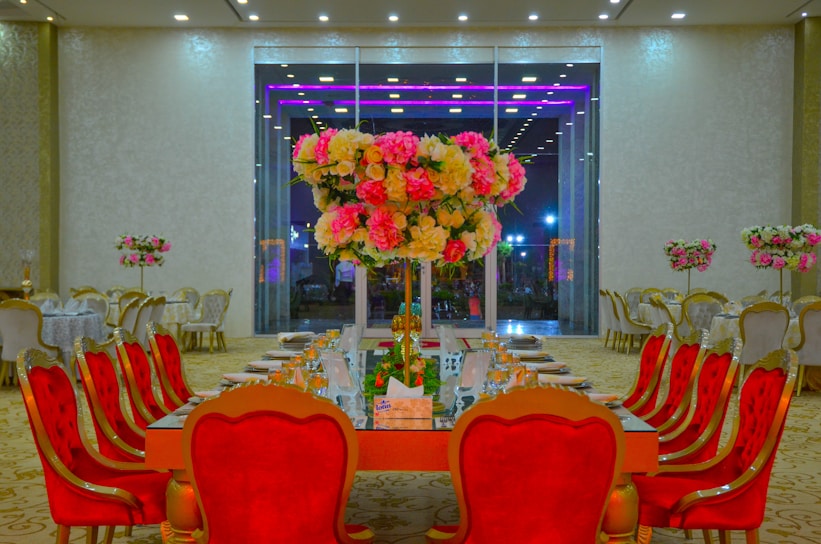 A beautifully decorated banquet hall with yellow and red floral arrangements and elegant table settings.