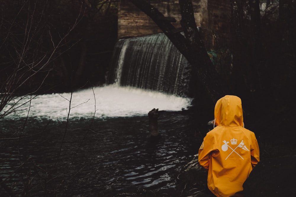 Persona in felpa gialla con cappuccio in piedi davanti alle cascate