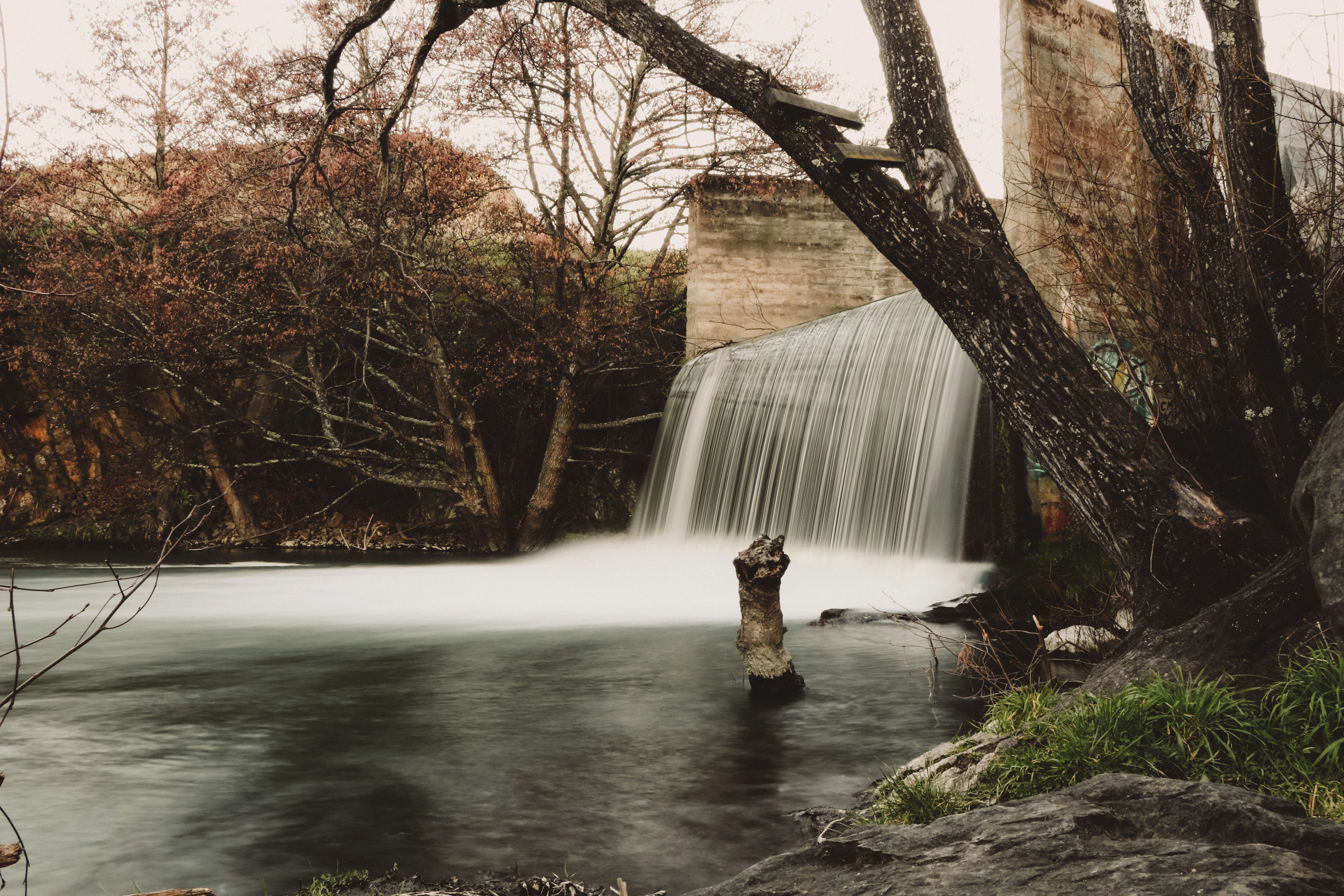 person in brown coat sitting on rock near water falls during daytime