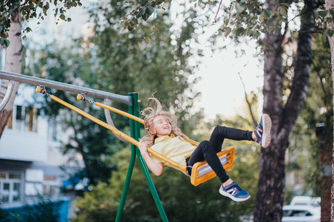 girl in black jacket and blue denim jeans sitting on swing during daytime