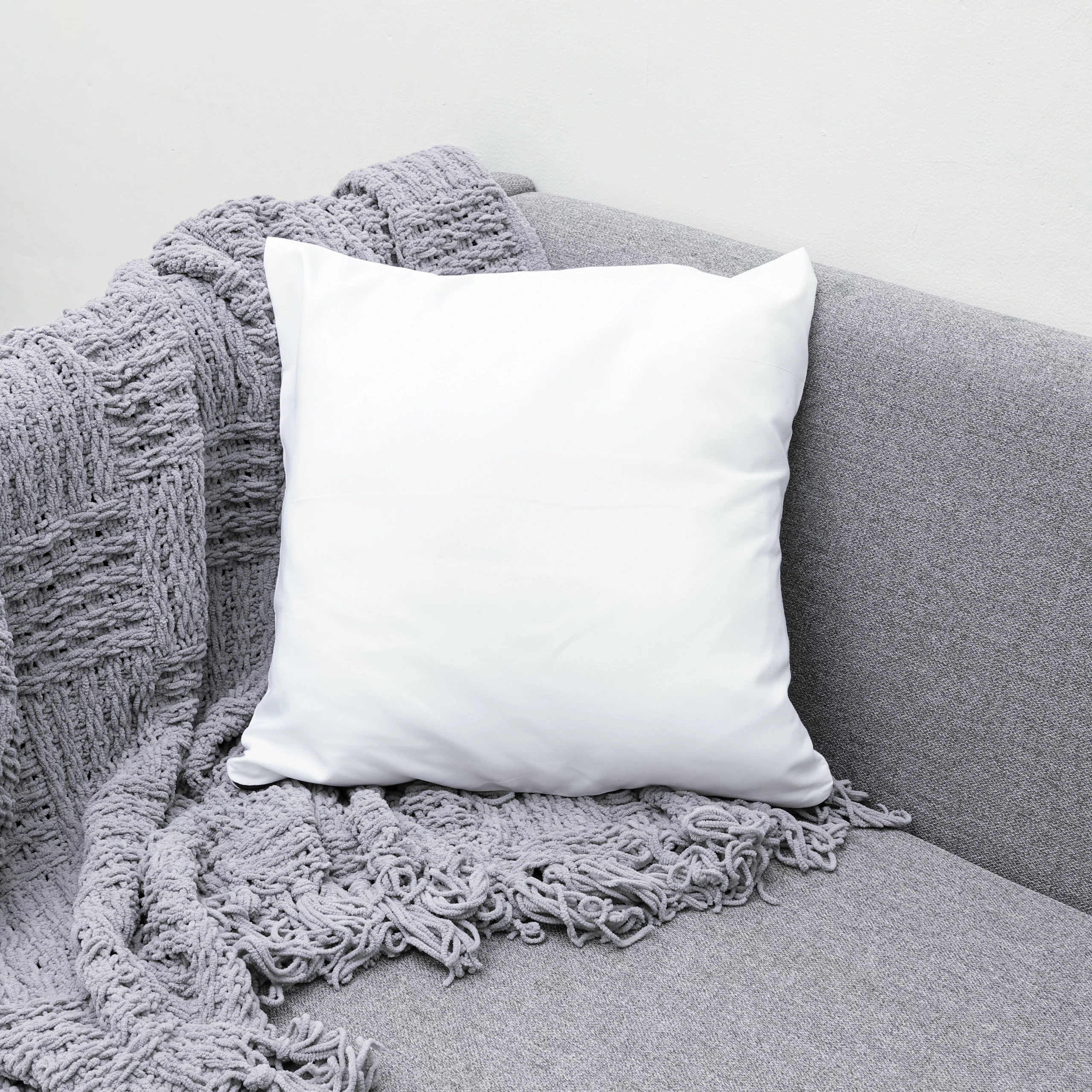 White cushion and knitted throw on a grey sofa