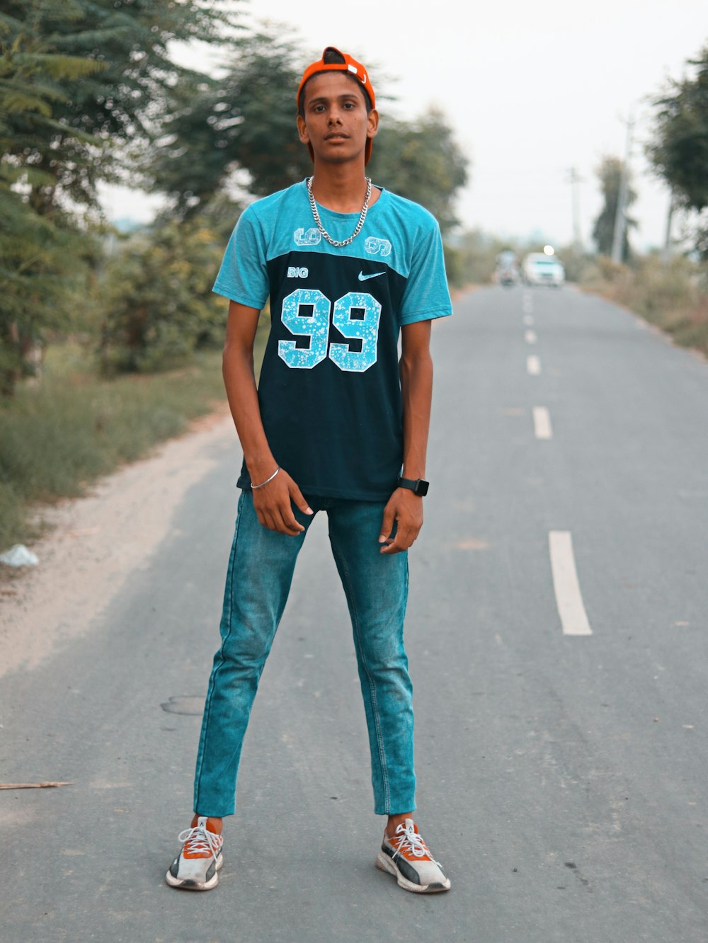 Hombre con camiseta azul de cuello redondo y jeans de mezclilla azul de pie en una carretera de asfalto gris