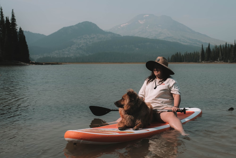 woman in black hat and white shirt sitting on red kayak on sea during daytime