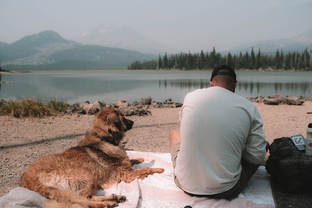 man in white long sleeve shirt sitting beside brown dog on brown sand during daytime