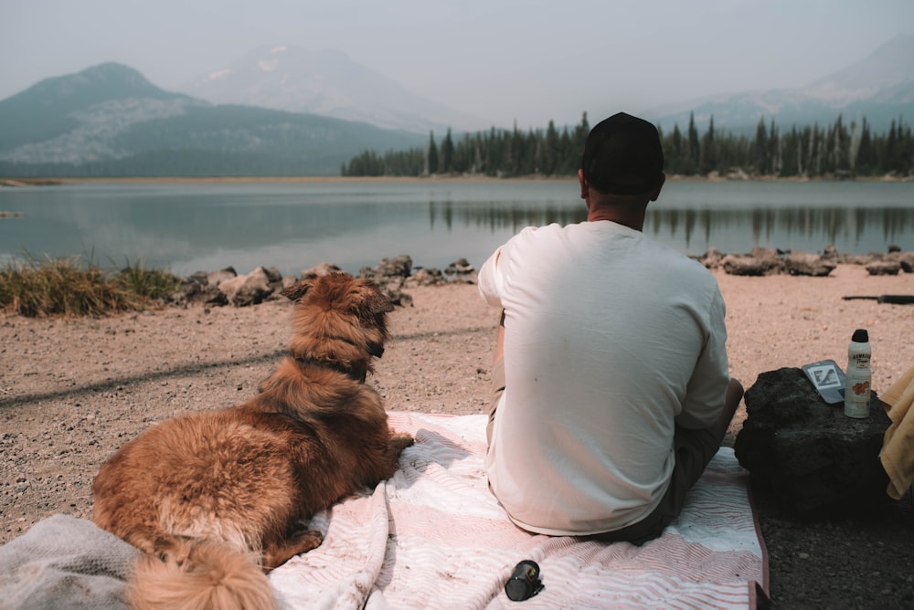 man in white dress shirt and black pants sitting beside brown dog on snow covered ground