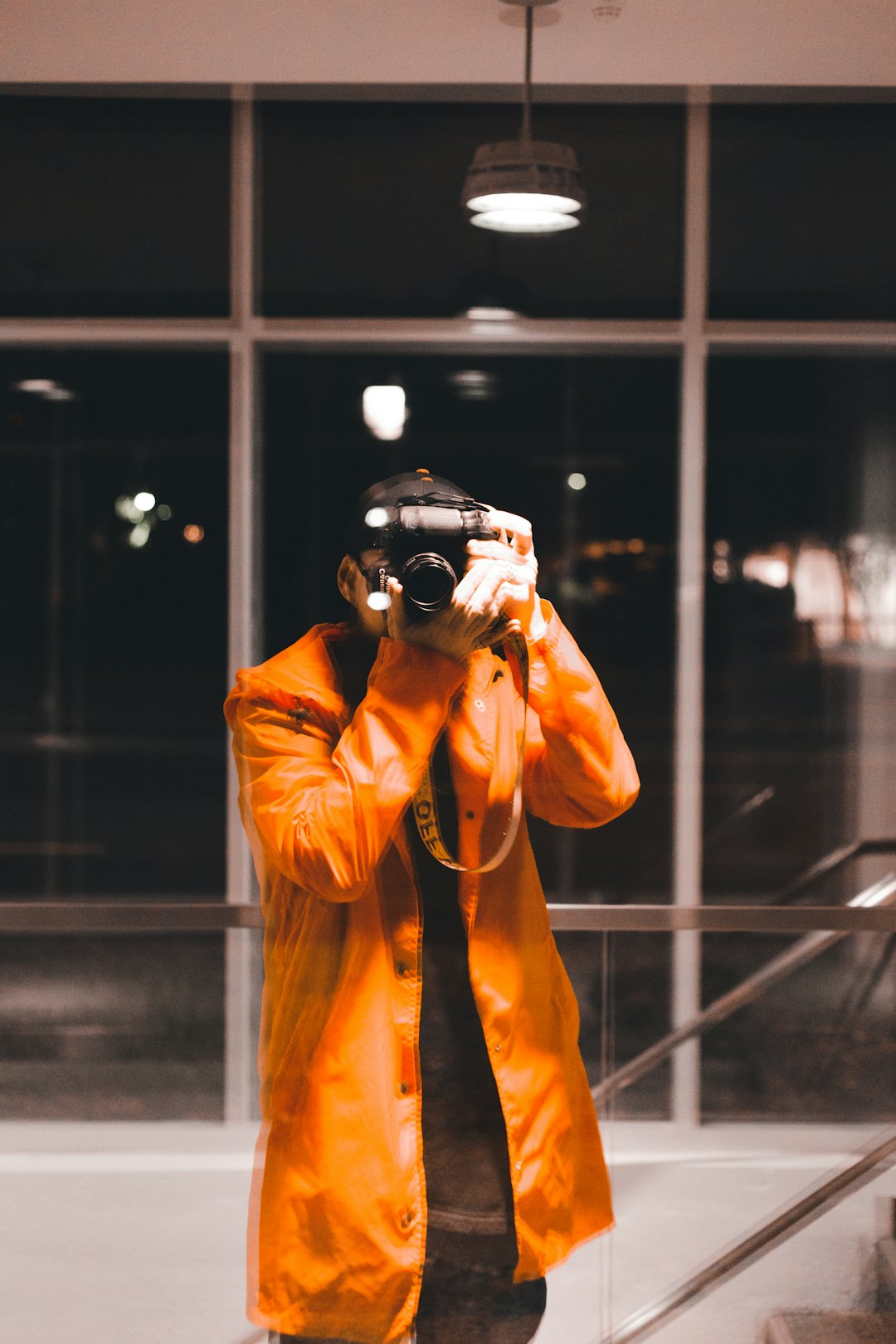 man in orange jacket holding black dslr camera