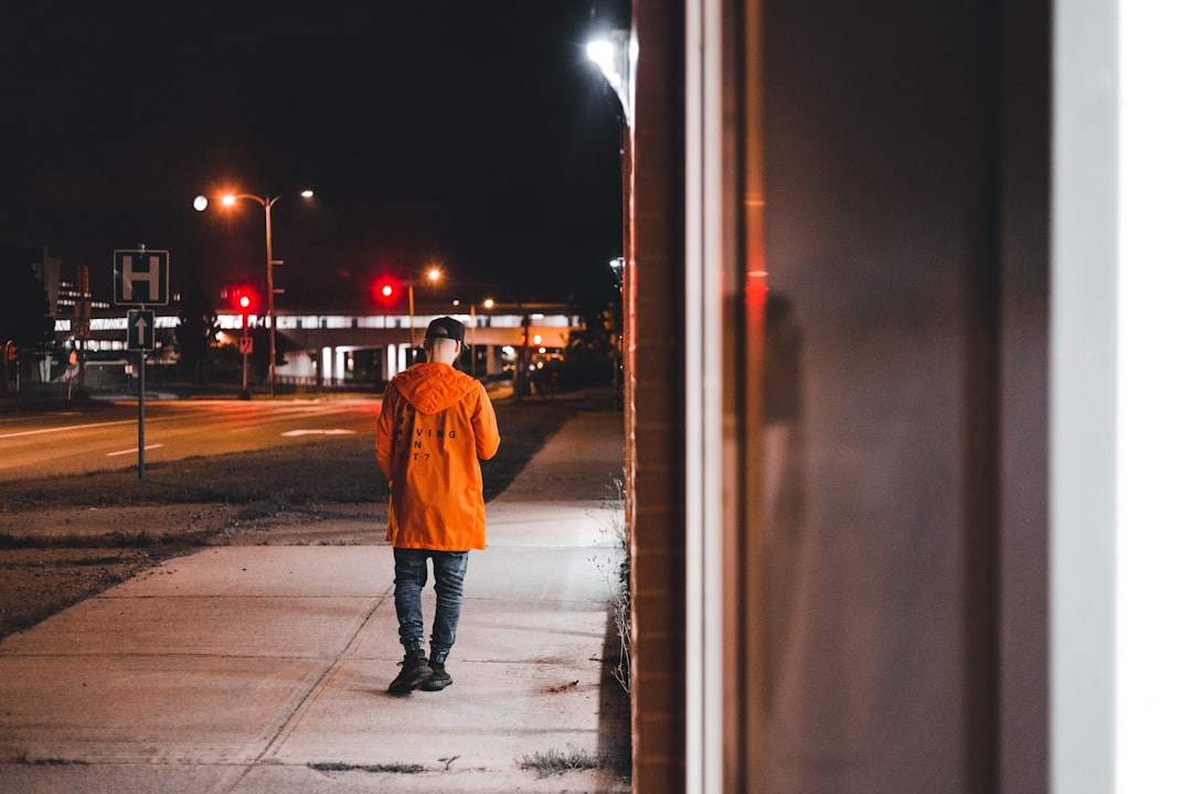 person in orange jacket walking on sidewalk during night time