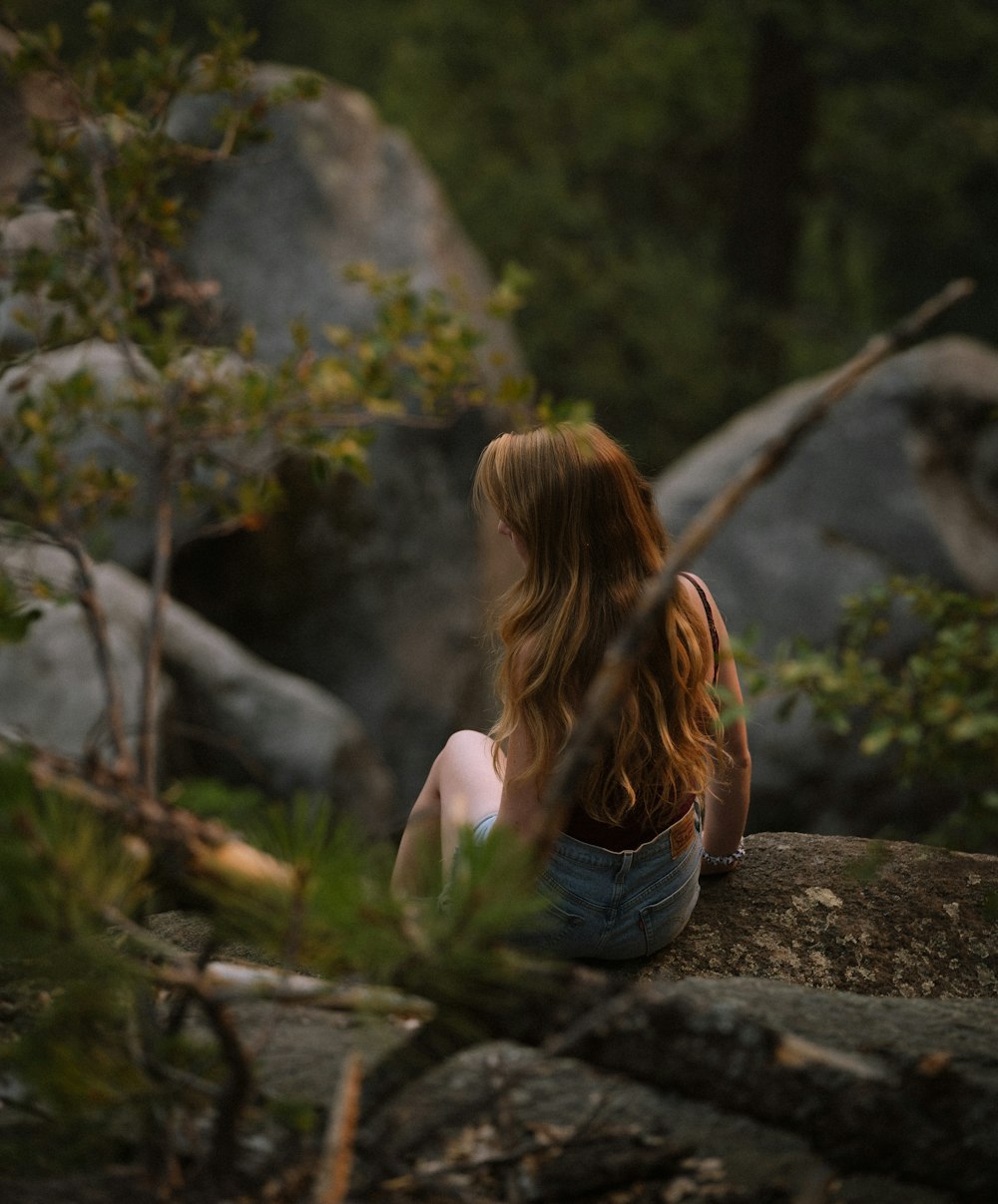 woman in black tank top and blue denim jeans sitting on rock during daytime