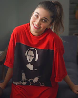 A person holding a custom-printed t-shirt with a bold graphic design, smiling in a cozy room.
