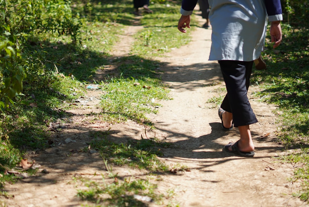 person in white shirt and black pants walking on dirt road during daytime