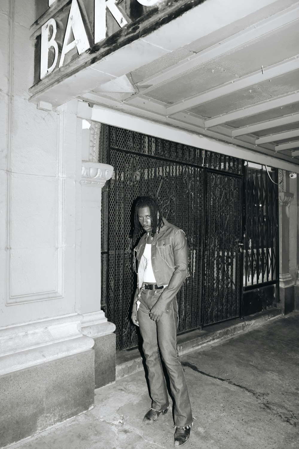 Hombre con camisa marrón abotonada y pantalones marrones de pie cerca de la puerta de metal negro durante el día