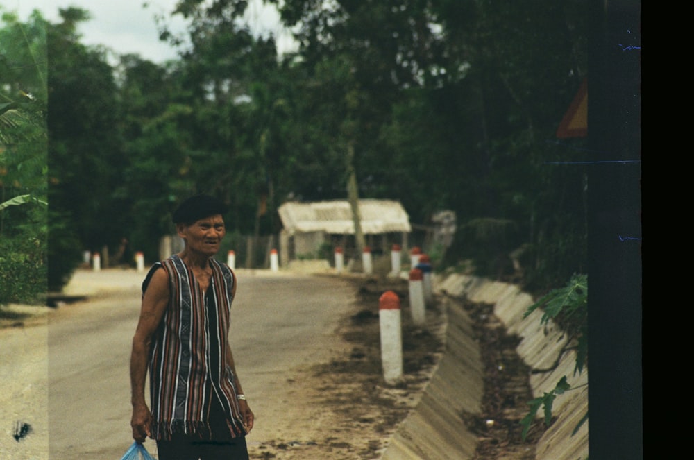 man in black and white stripe tank top standing on dirt road during daytime