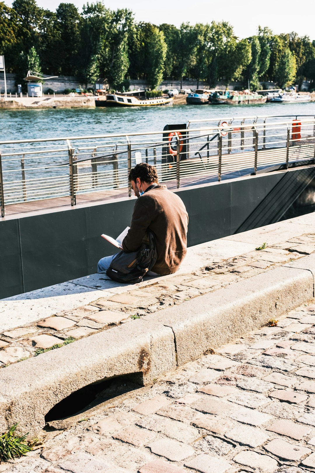 man in brown jacket sitting on concrete dock during daytime
