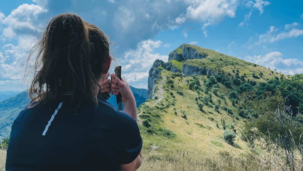 woman in blue t-shirt taking photo of green mountain during daytime