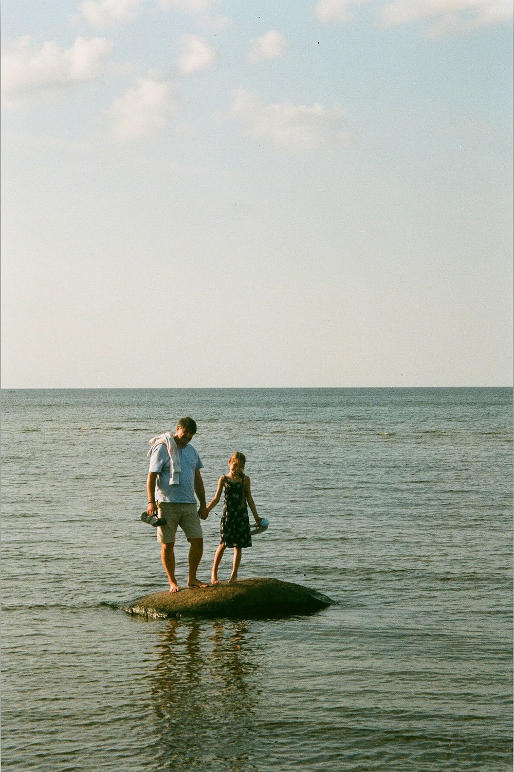 man and woman standing on rock in the middle of the sea