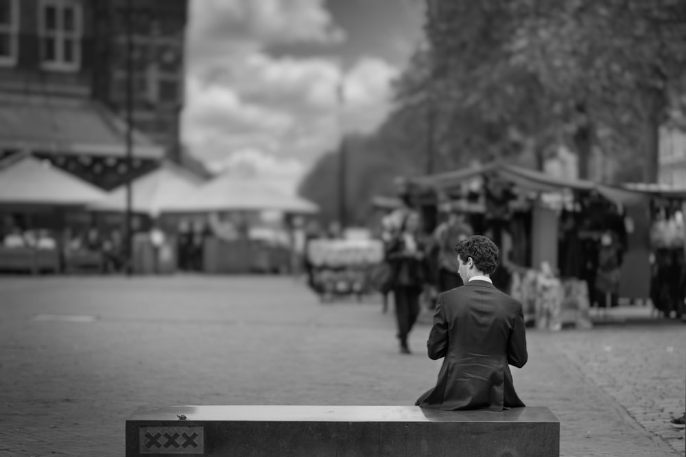 foto en escala de grises de un hombre con traje negro sentado en un banco