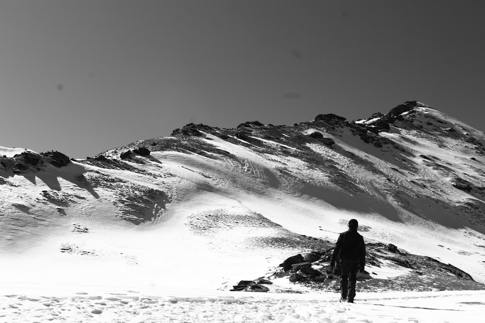 grayscale photo of man standing on rock formation near body of water