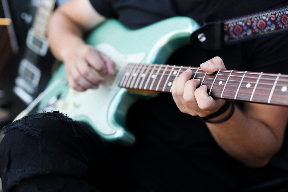 person playing white and black stratocaster electric guitar