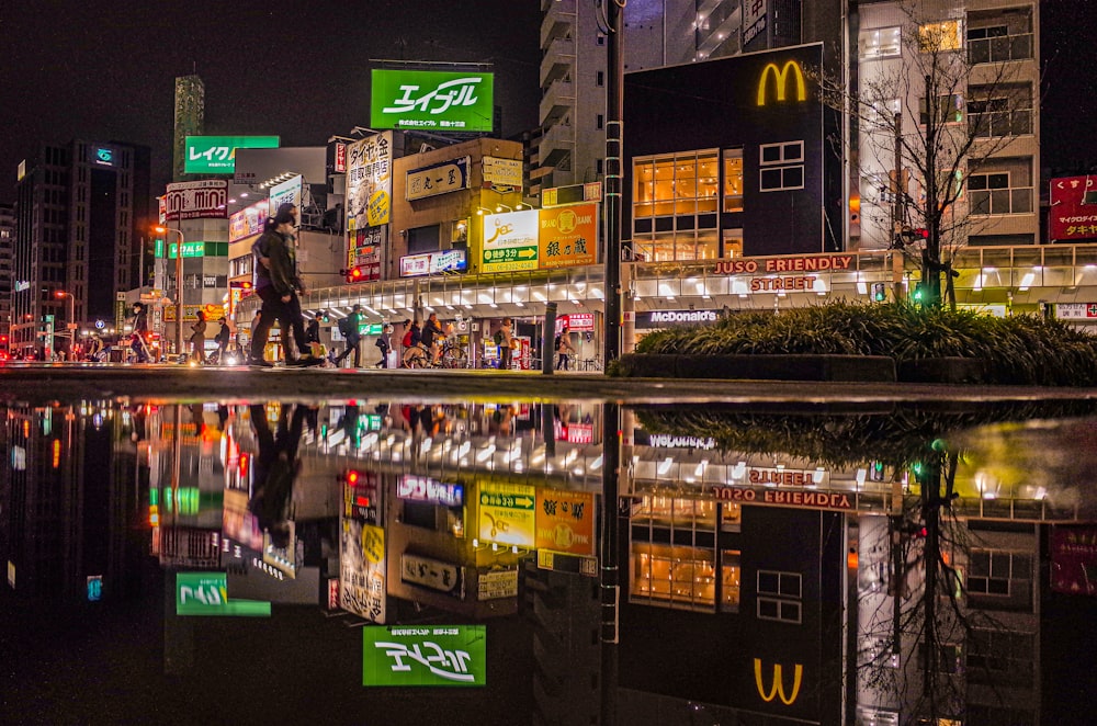 a city at night with people walking on the sidewalk