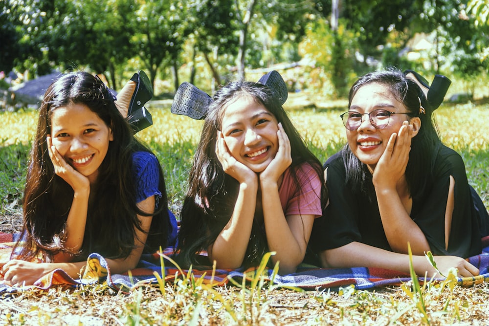 3 women sitting on grass field during daytime