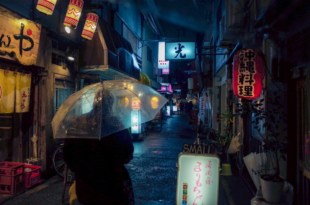pessoa na jaqueta preta segurando o guarda-chuva andando na rua durante a noite