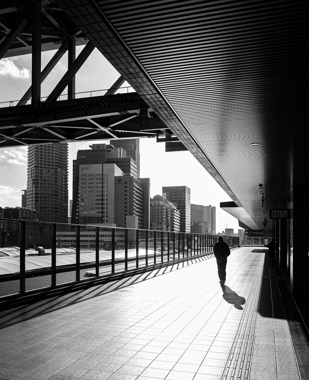 grayscale photo of woman walking on sidewalk