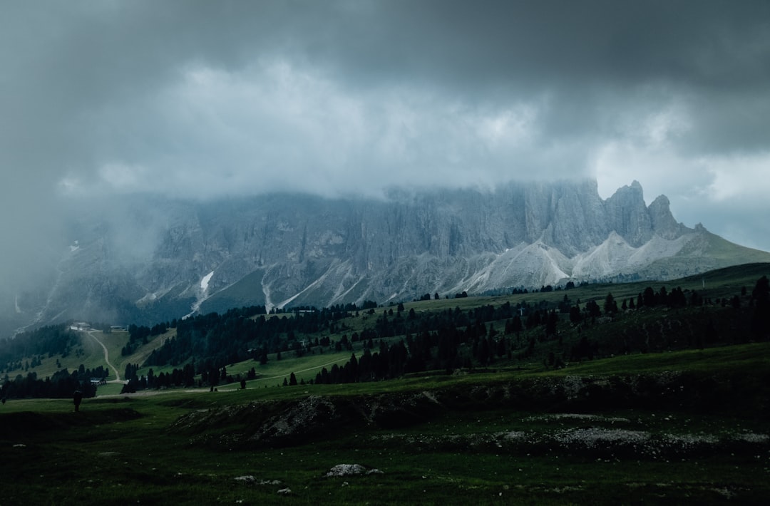 green grass field near mountain under white clouds during daytime