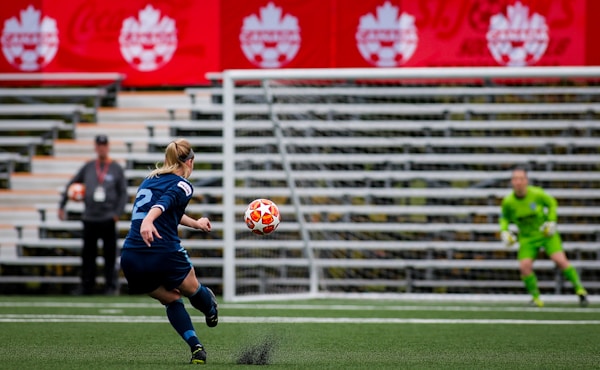 Young women shooting the soccer ball towards the goal.  The soccer goalkeeper is moving to her right in preparation to save the shot. Football Manager looks on.by My Profit Tutor