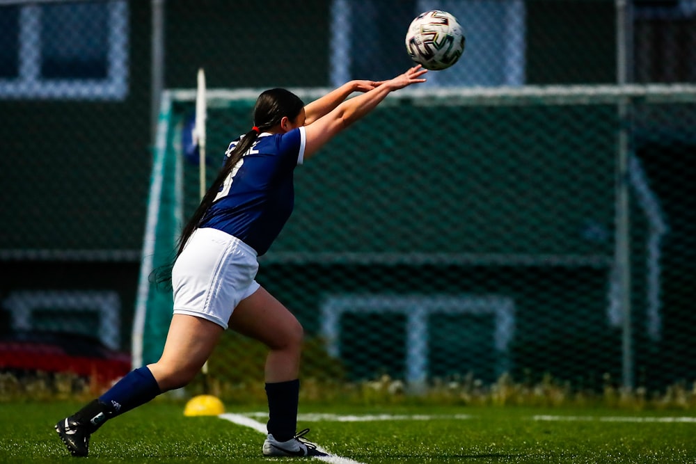 woman in blue and white jersey shirt and white shorts playing soccer during daytime
