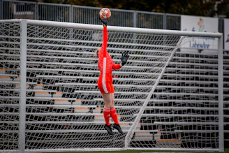 man in red jersey shirt and black pants playing soccer