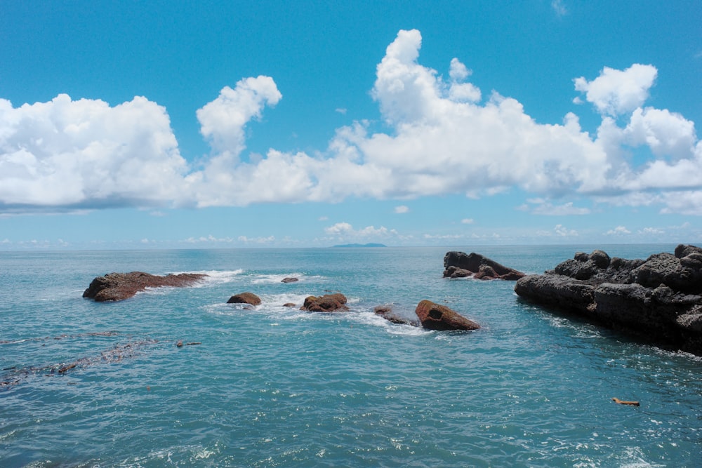 Formazione rocciosa marrone sul mare sotto cielo blu e nuvole bianche durante il giorno